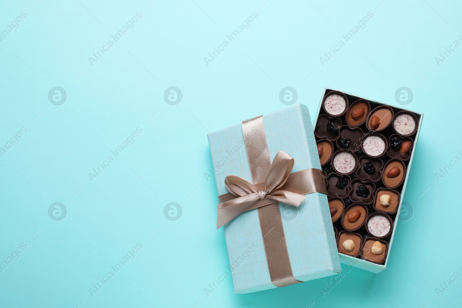 Photo of Open box of delicious chocolate candies on light blue background, flat lay. Space for text