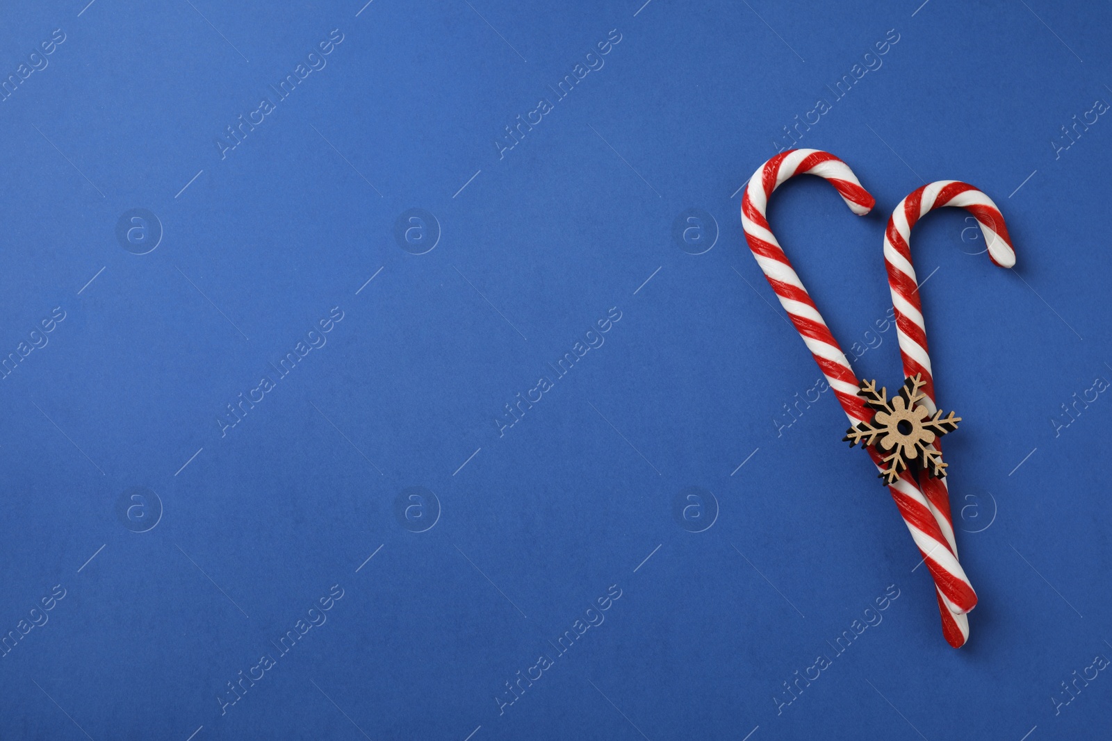 Photo of Flat lay composition with candy canes and snowflake on blue background. Space for text