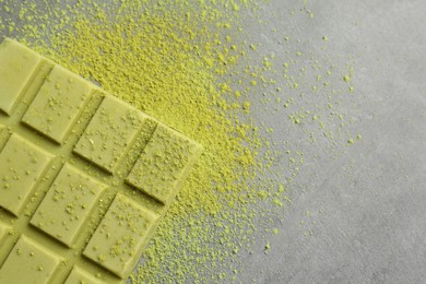 Photo of Tasty matcha chocolate bar and powder on grey textured table, top view. Space for text