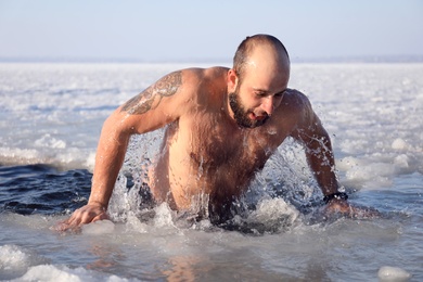 MYKOLAIV, UKRAINE - JANUARY 06, 2021: Man getting out of ice hole on winter day