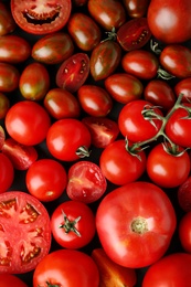 Many fresh ripe whole and cut tomatoes as background, top view