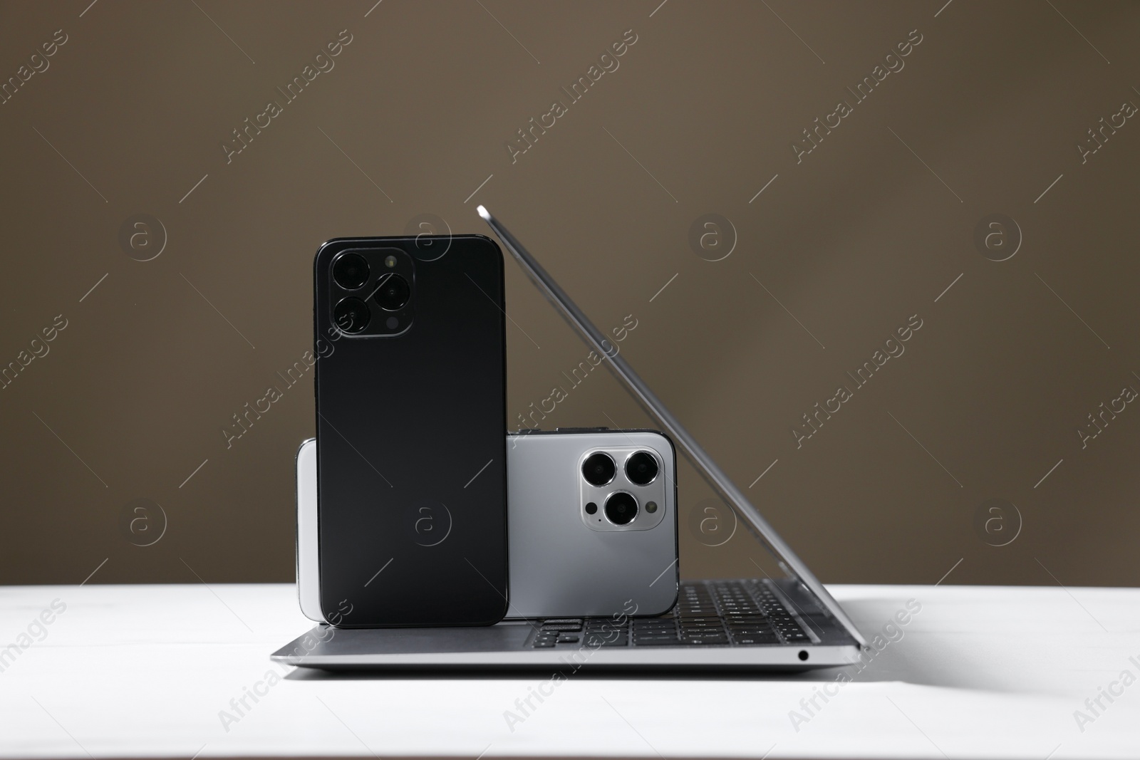 Photo of Modern laptop and smartphones on white table against brown background. Space for text