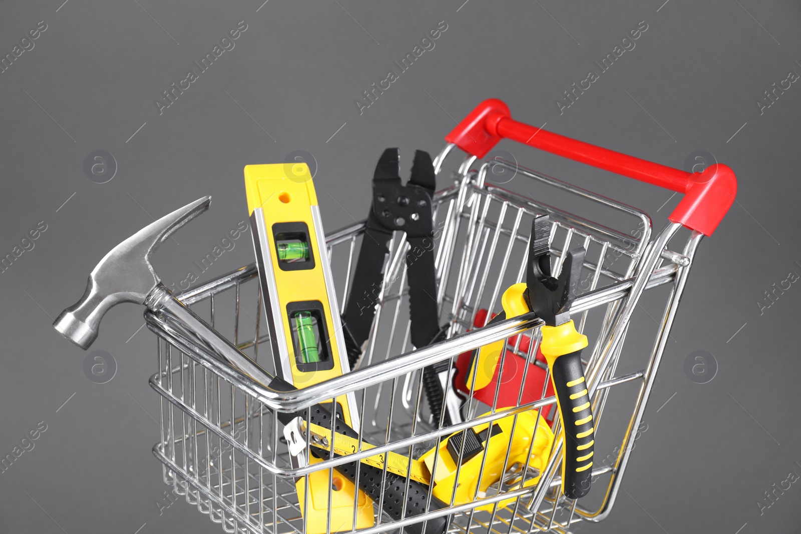 Photo of Small shopping cart with set of construction tools on grey background, closeup