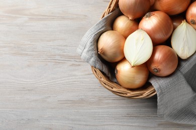 Photo of Wicker basket with whole and cut onions on light grey wooden table, top view. Space for text