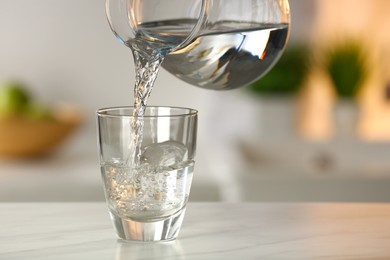 Pouring water from jug into glass on white marble table in kitchen. Space for text