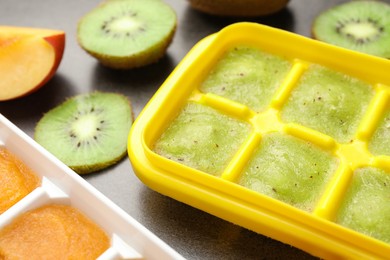 Photo of Nectarine and kiwi puree in ice cube tray with ingredients on grey table, closeup