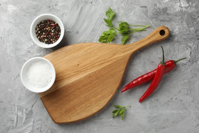 Photo of Cutting board, salt, spices, chili peppers and parsley on grey textured table, flat lay. Space for text