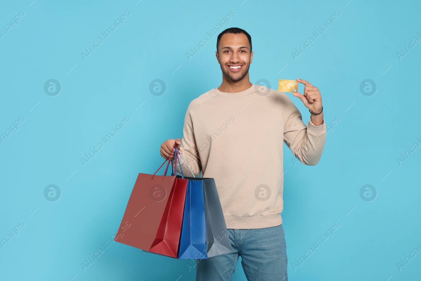 Photo of Happy African American man with shopping bags and credit card on light blue background