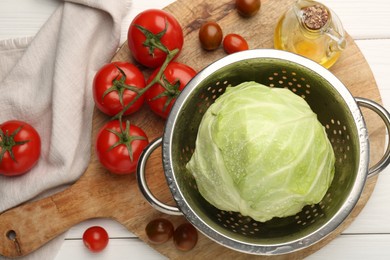 Photo of Wet cabbage in colander, oil and tomatoes on white wooden table, top view