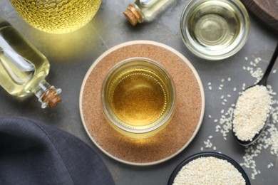 Sesame oil and seeds on grey table, flat lay