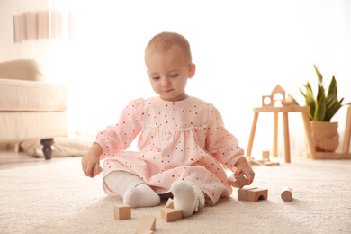 Cute child playing with wooden building blocks on floor at home