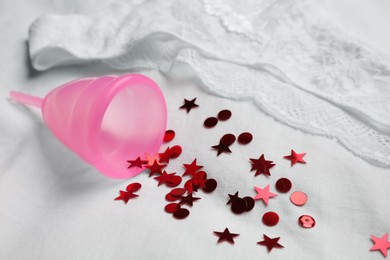 Photo of Woman's panties and menstrual cup with red confetti on white fabric