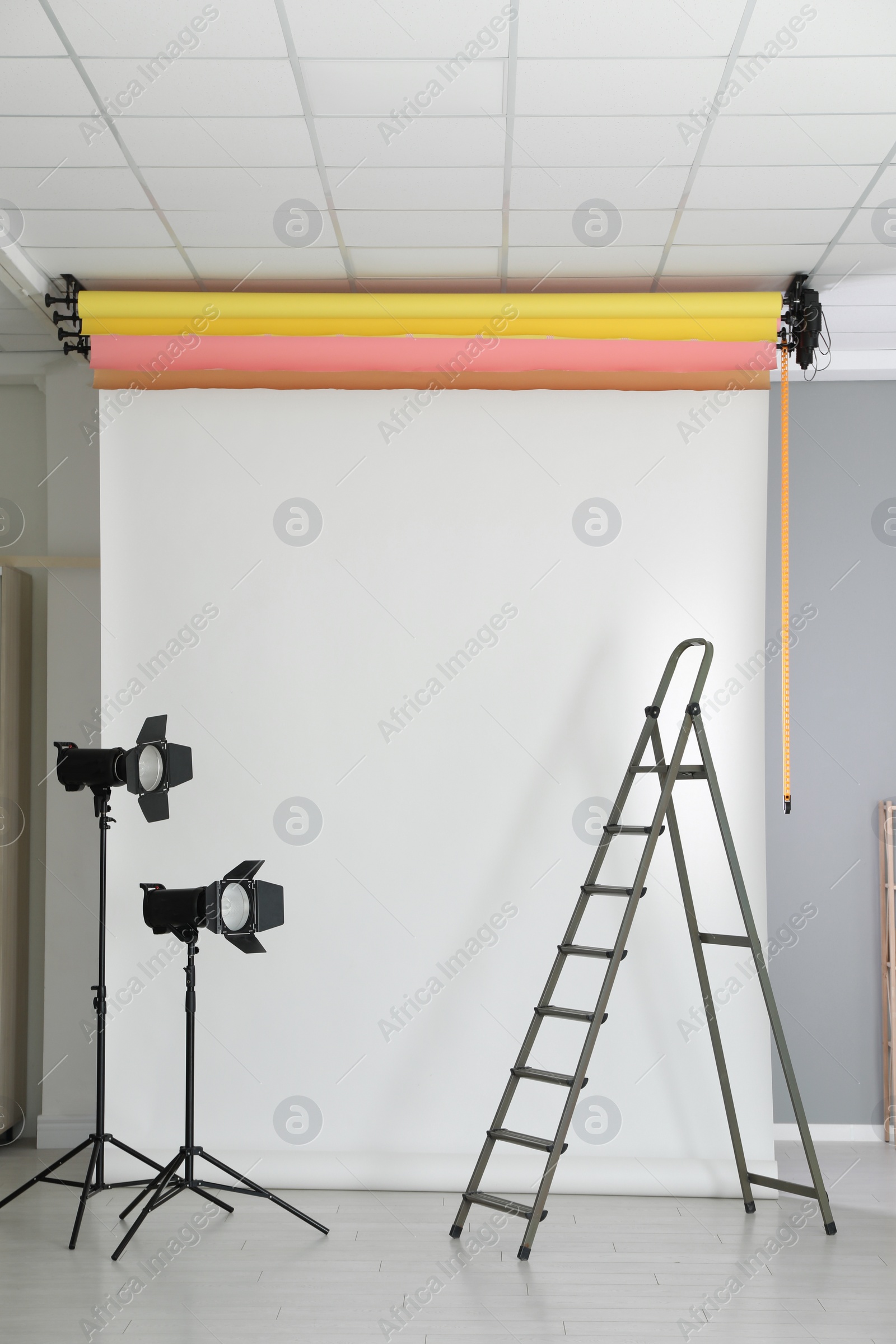 Photo of White photo background, ladder and professional lighting equipment in modern studio