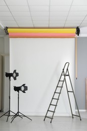 Photo of White photo background, ladder and professional lighting equipment in modern studio