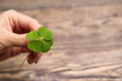 Photo of Woman holding green four leaf clover on wooden background, closeup. Space for text