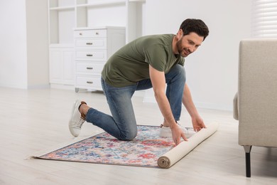 Smiling man unrolling carpet with beautiful pattern on floor in room, closeup