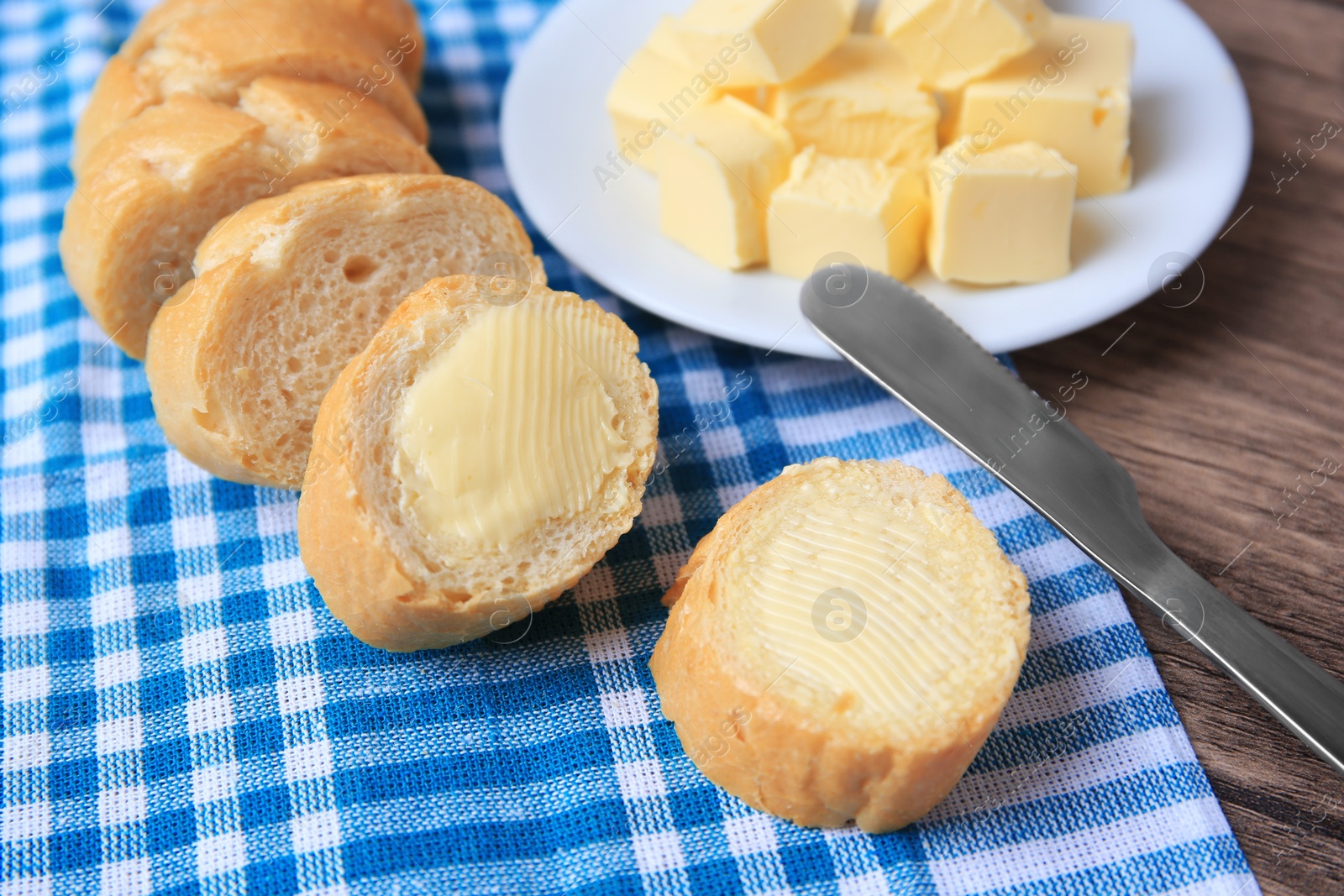 Photo of Tasty cut baguette with fresh butter on wooden table, closeup