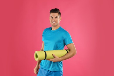 Handsome man with yoga mat on pink background