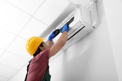 Photo of Male technician checking air conditioner indoors