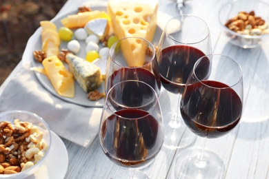 Photo of Red wine and snacks served for picnic on white wooden table outdoors