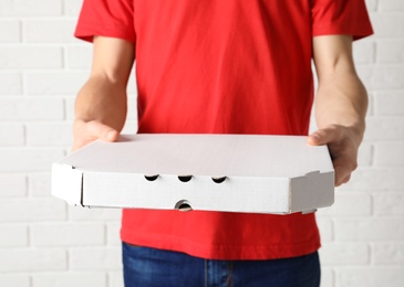 Photo of Young man with pizza box near white brick wall. Food delivery service