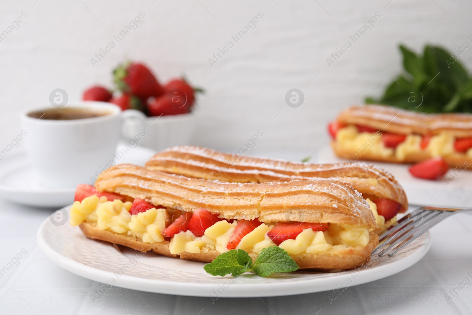 Photo of Delicious eclairs filled with cream, strawberries and mint on white table