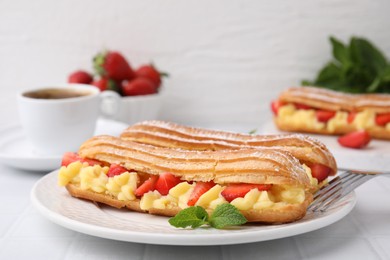 Photo of Delicious eclairs filled with cream, strawberries and mint on white table