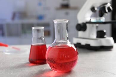 Laboratory analysis. Flasks with red liquid, petri dish and microscope on light grey table