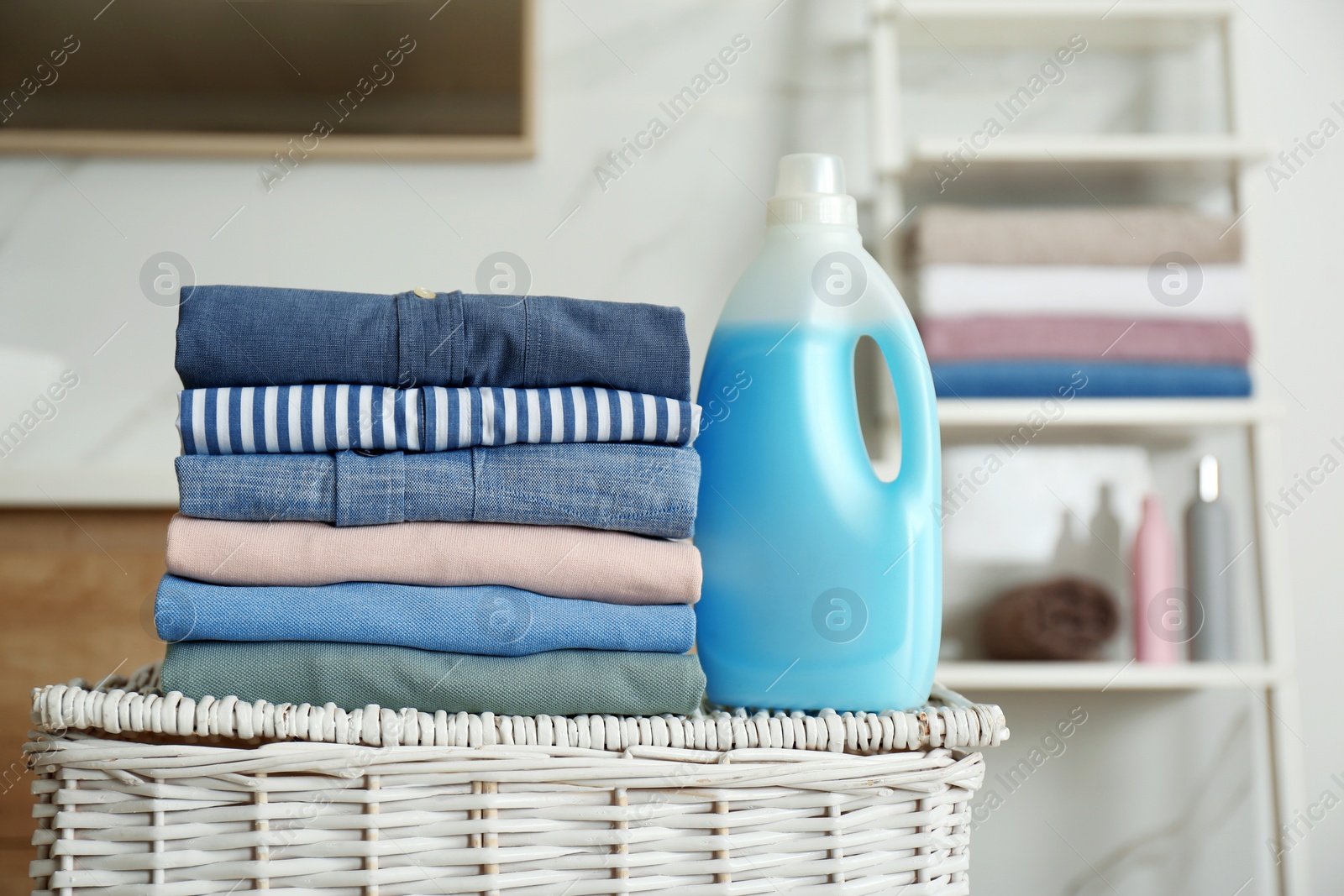 Photo of Stack of fresh laundry and detergent on basket in bathroom