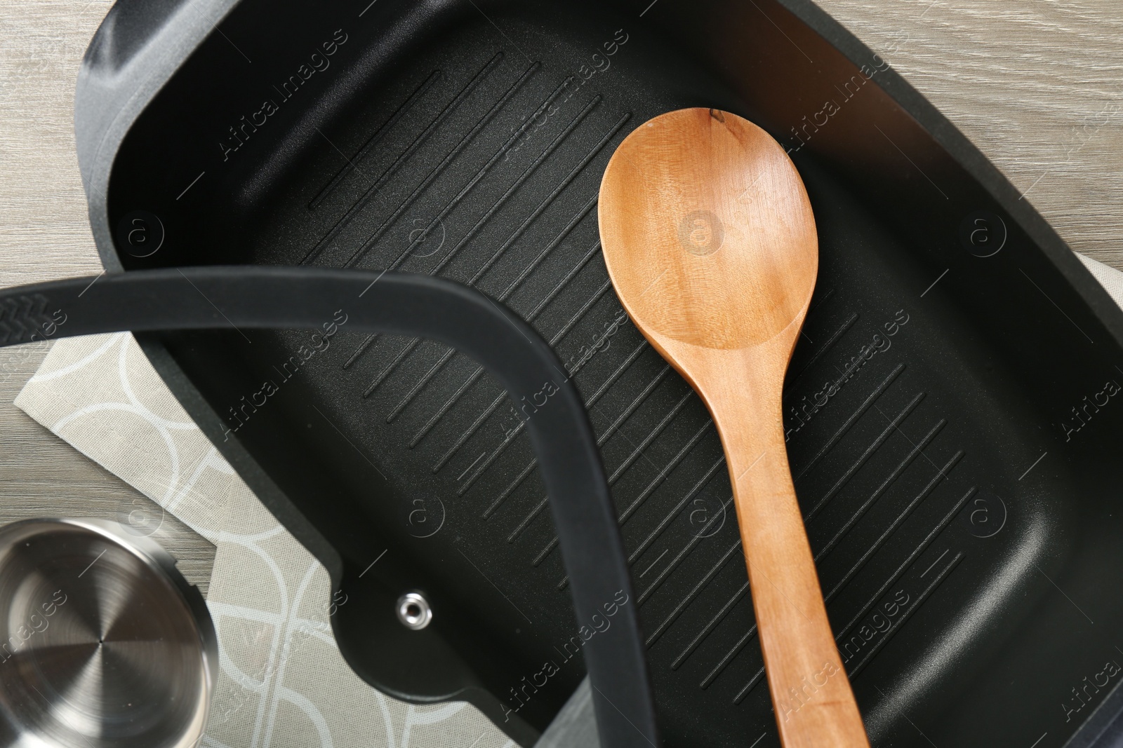 Photo of Black pot with glass lid and spoon on wooden table, top view