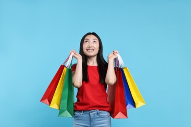 Happy woman with shopping bags on light blue background