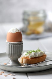 Fresh soft boiled egg in cup and sandwich on white wooden table