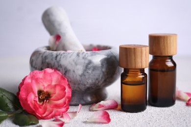 Photo of Glass bottles of aromatic essential oil, mortar with roses on white table, closeup