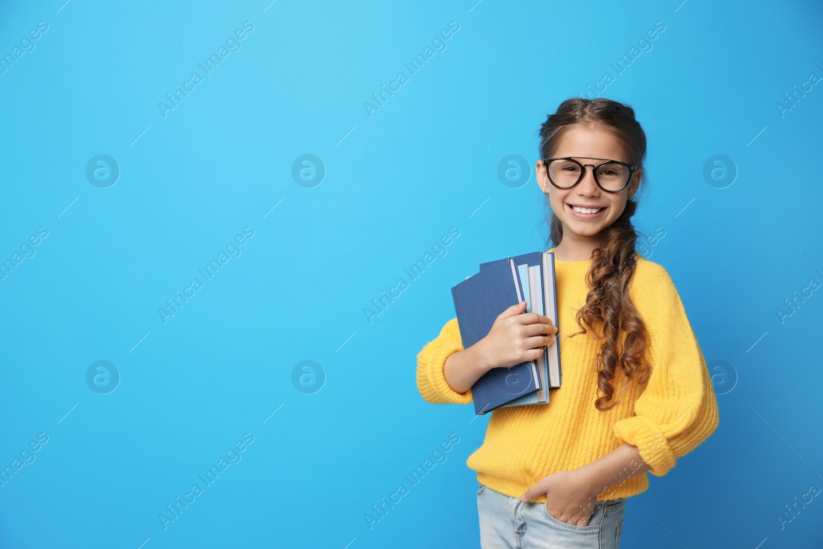 Photo of Cute little girl with glasses and books on blue background, space for text. Reading concept