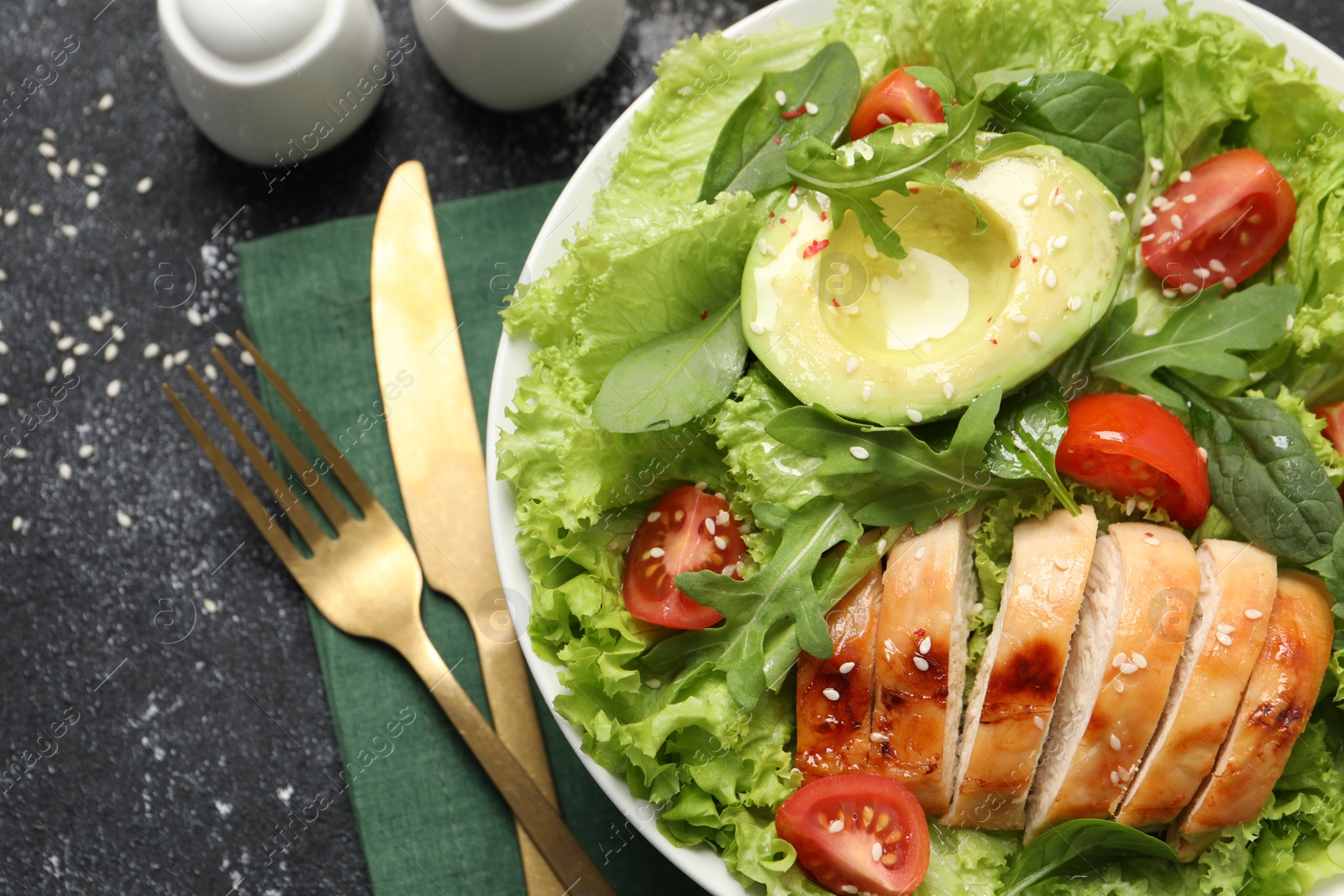 Photo of Delicious salad with chicken, cherry tomato and avocado served on grey textured table, flat lay