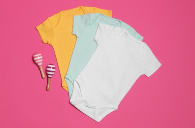 Baby bodysuits and maracas on pink background, flat lay