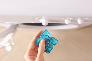 Photo of Woman holding laundry detergent capsule near washing machine indoors, top view