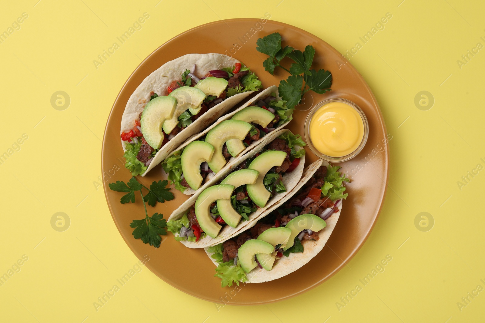 Photo of Delicious tacos with meat, vegetables and avocado served on yellow table, top view