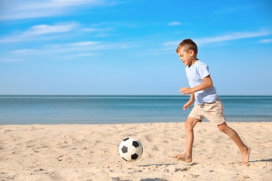 Photo of Cute little boy playing with football ball on sandy beach