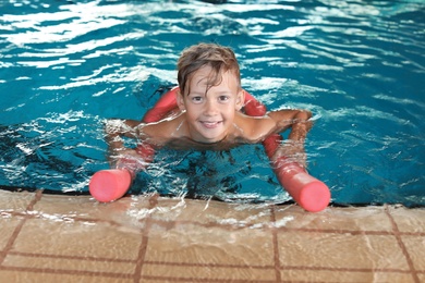 Photo of Little boy with swimming noodle in indoor pool