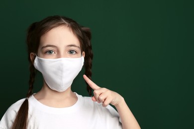 Photo of Girl wearing protective mask on green background, space for text. Child's safety from virus