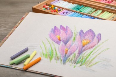 Photo of Beautiful drawing of crocus flowers and pastels on wooden table