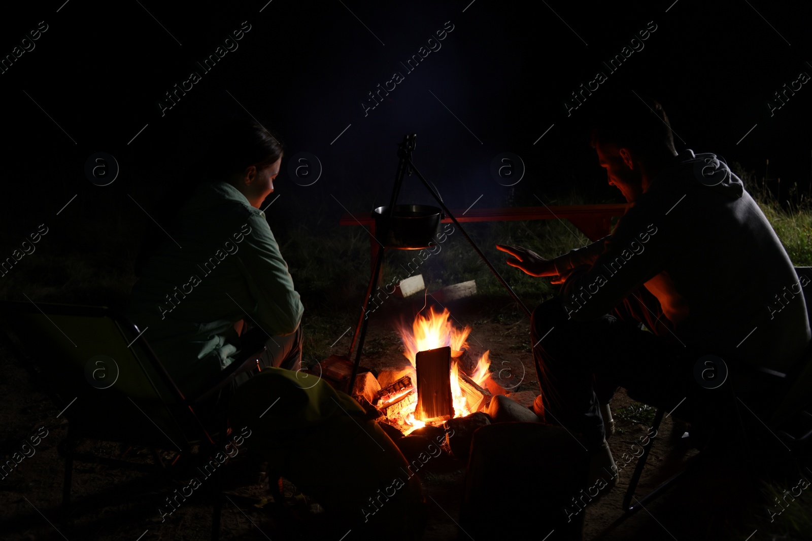 Photo of Couple sitting near bonfire in camp at night