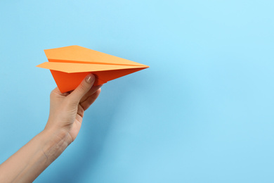 Woman holding paper plane on light blue background, closeup. Space for text