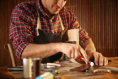 Photo of Man marking leather with roller in workshop, closeup