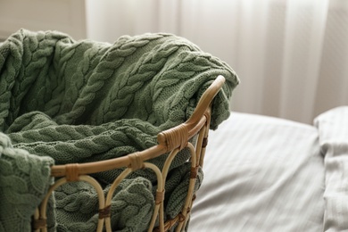 Photo of Knitted green plaid in wicker basket on bed indoors, closeup