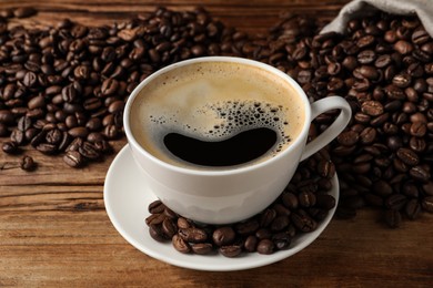 Cup of aromatic hot coffee and beans on wooden table