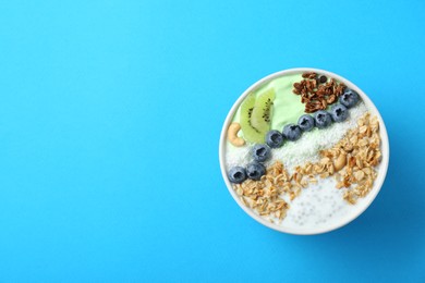 Photo of Tasty smoothie bowl with fresh kiwi fruit, blueberries and oatmeal on light blue background, top view. Space for text
