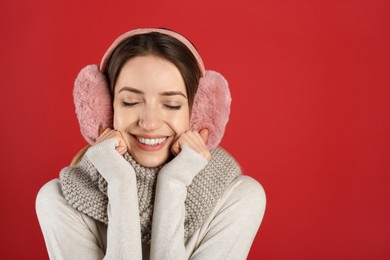 Happy woman wearing warm earmuffs on red background, space for text