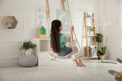 Cute little girl playing on swing at home, back view